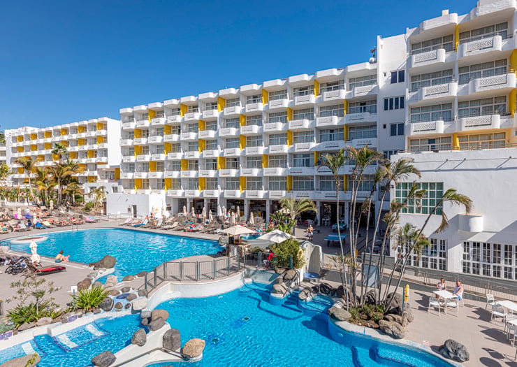 Complejo hotelero moderno de apartamentos blancos con balcones amarillos y piscina turquesa