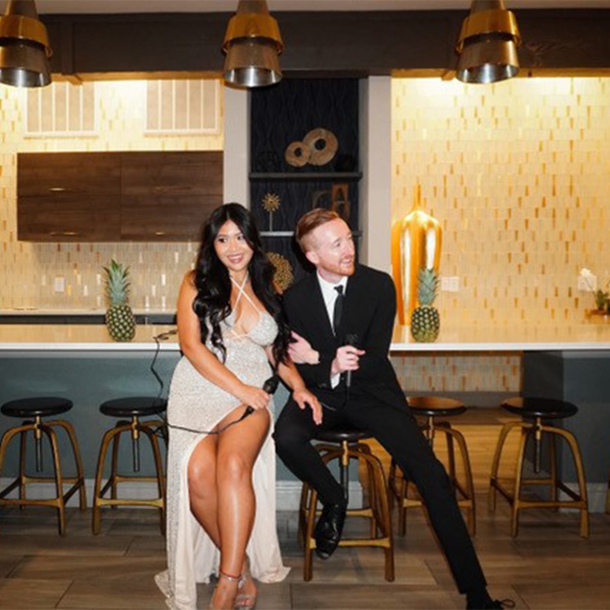 Couple in formal attire posing at modern bar with gold pendant lights and pineapple decorations