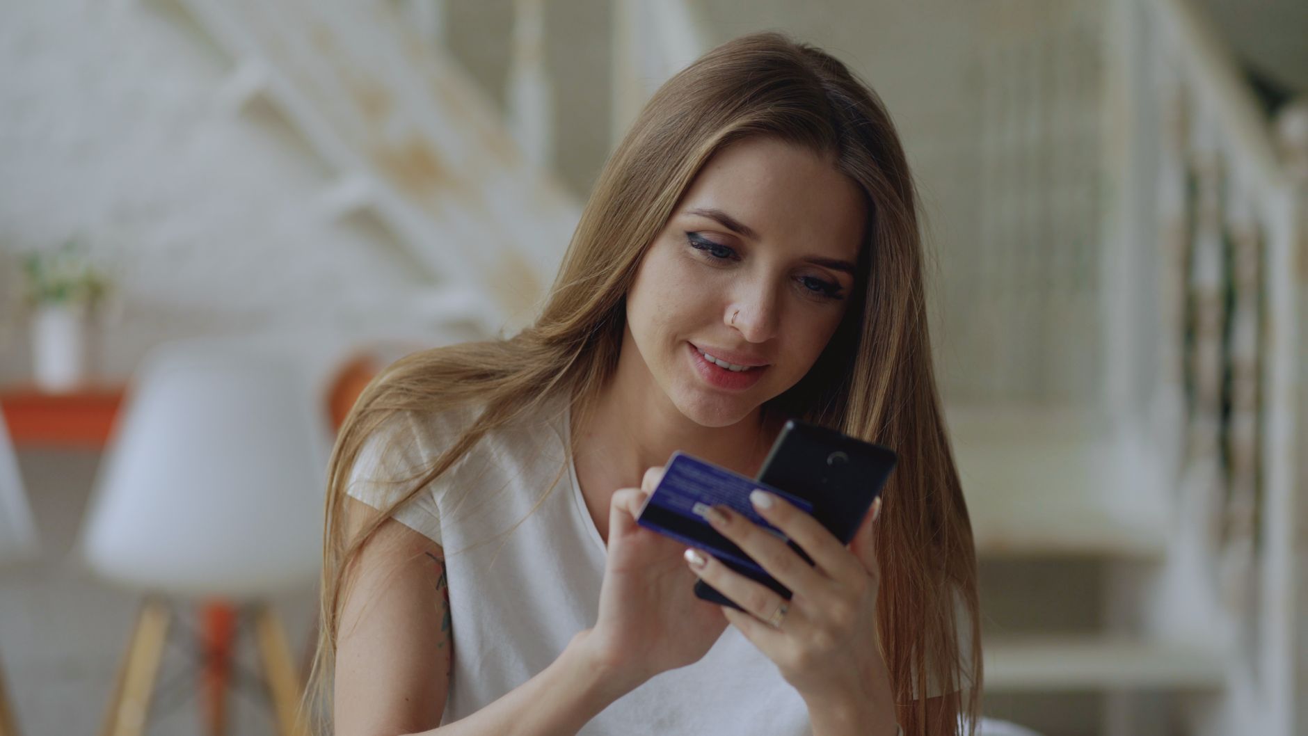 Kobieta w białej koszulce uśmiecha się patrząc na smartfon z niebieskim etui w dłoniach