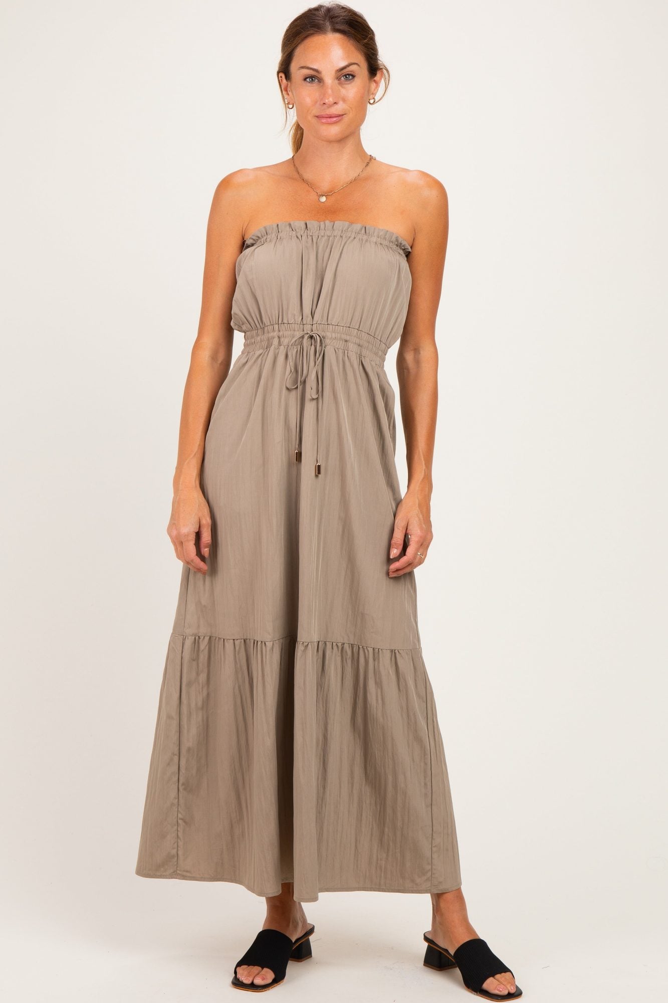 Pregnant woman in beige strapless maternity dress with empire waist and ruffled hem, standing facing forward