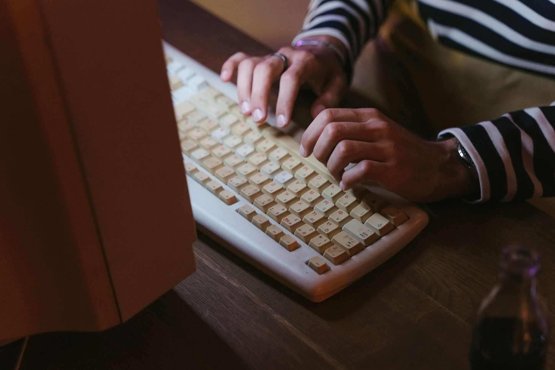 Child's hands typing on a beige keyboard at a wooden desk