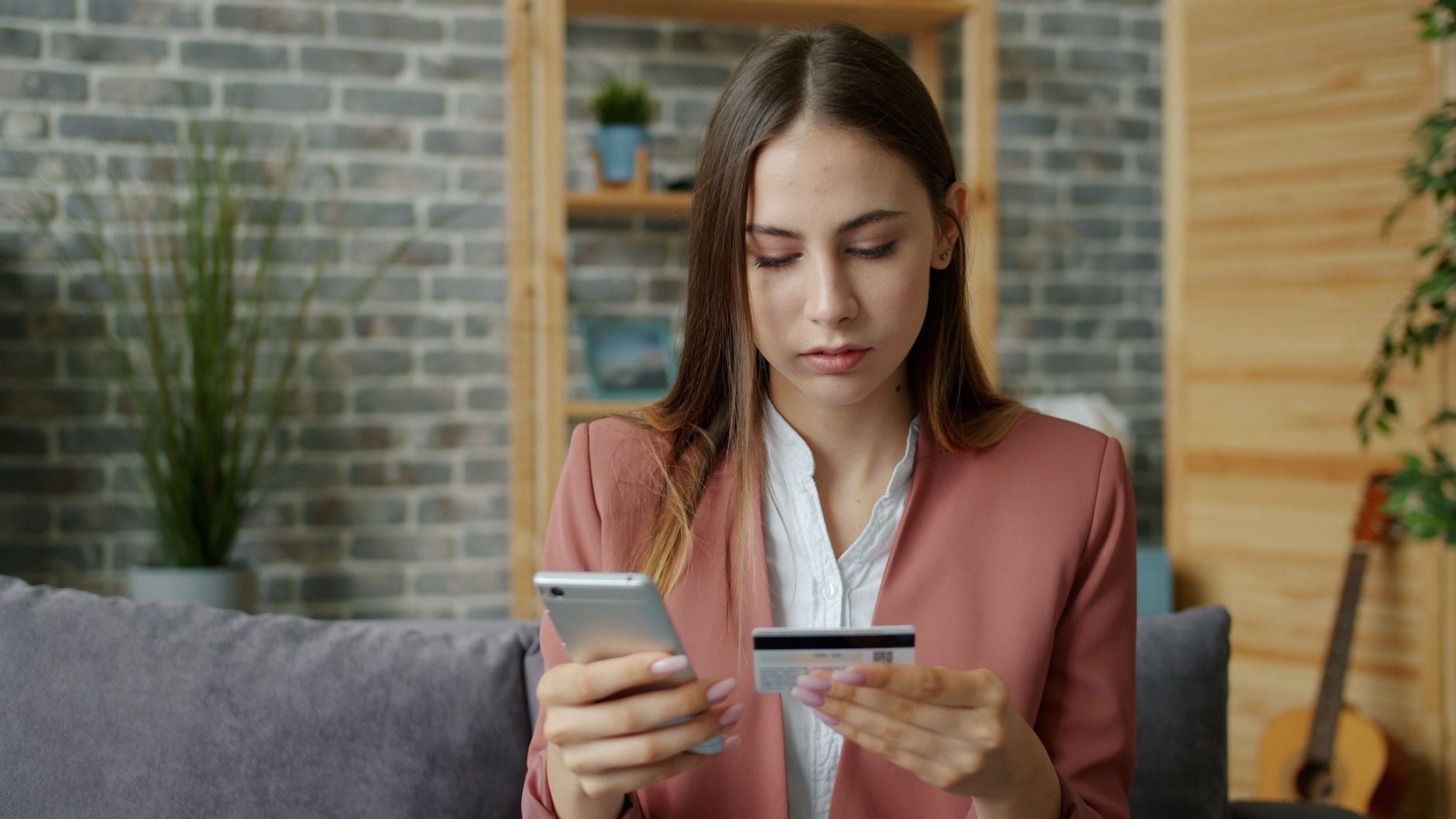 Kobieta w różowej marynarce trzyma tablet i kartę kredytową siedząc na kanapie