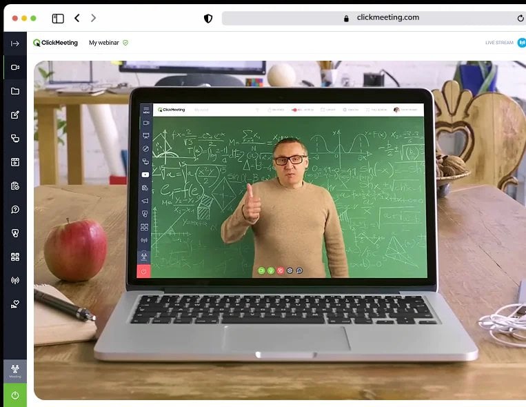 Mężczyzna w beżowym swetrze podczas webinaru z zieloną tablicą pełną równań matematycznych na tle