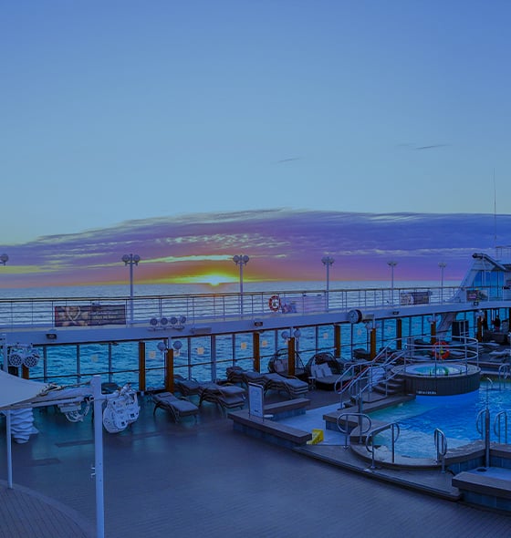 Sunset over cruise ship pool deck with lounge chairs and colorful sky