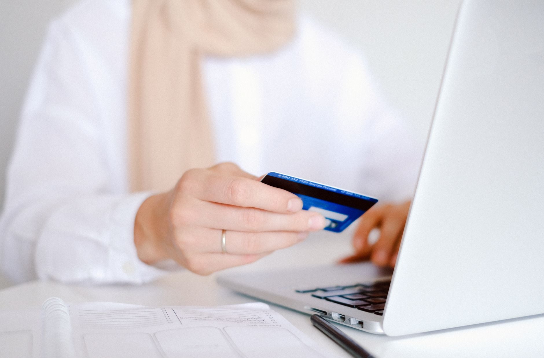 Kobieta w białej koszuli trzymająca niebieską kartę kredytową przed laptopem podczas dokonywania płatności online