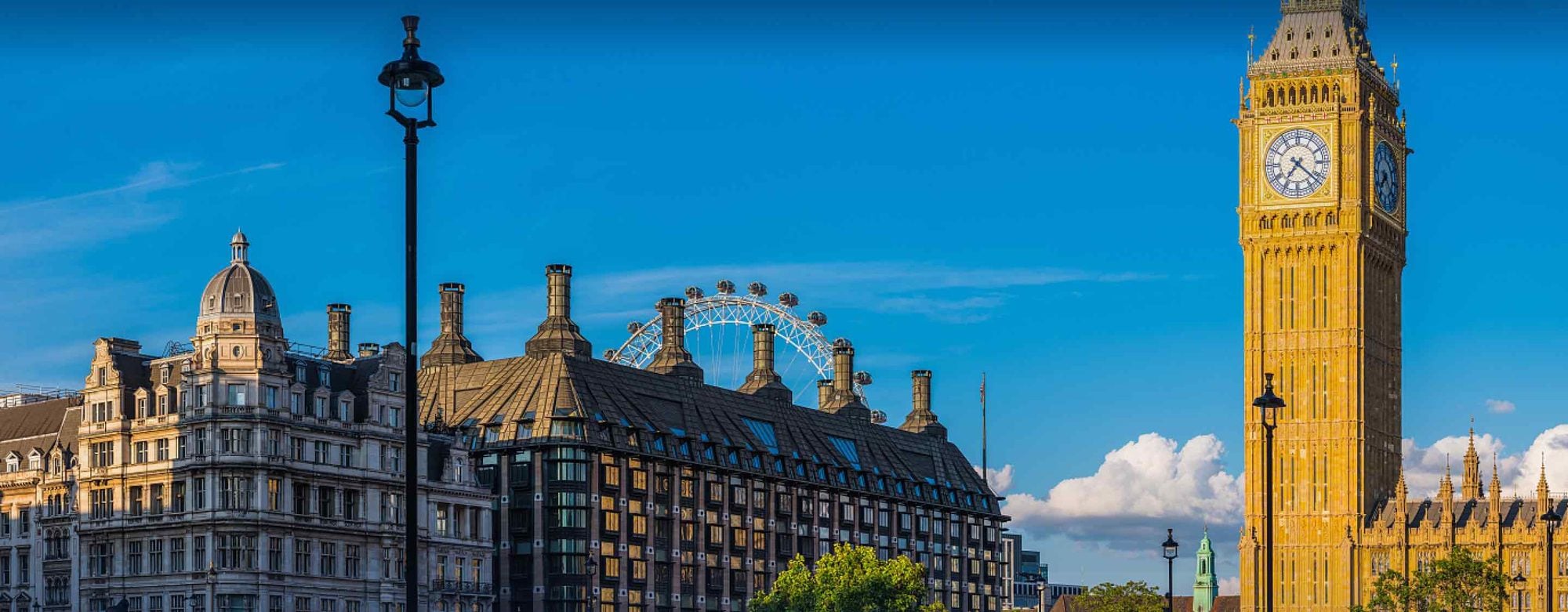 London skyline featuring Big Ben, the London Eye, and historic Victorian architecture under a clear blue sky