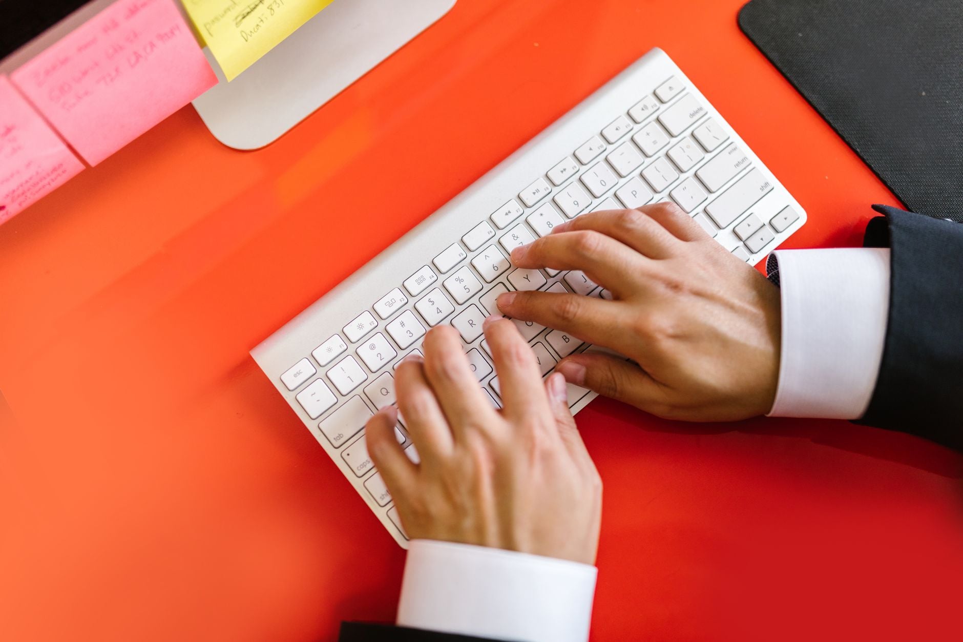 Adult hands typing on a white keyboard on a bright orange desk surface