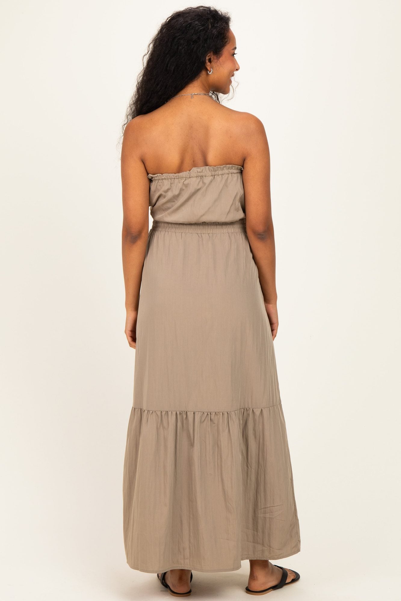 Back view of pregnant woman wearing beige strapless maternity dress with tiered skirt and drawstring waist